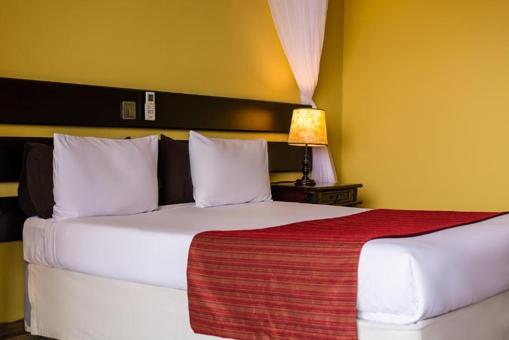 a bedroom with a large white bed with a lamp at Cassia Lodge in Munyonyo