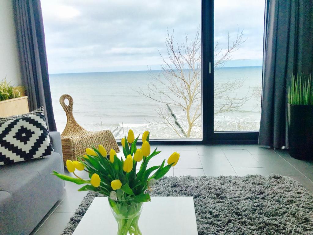 a vase with yellow flowers on a table in front of a window at Apartment Morski Widok w Boulevard Ustronie Morskie in Ustronie Morskie