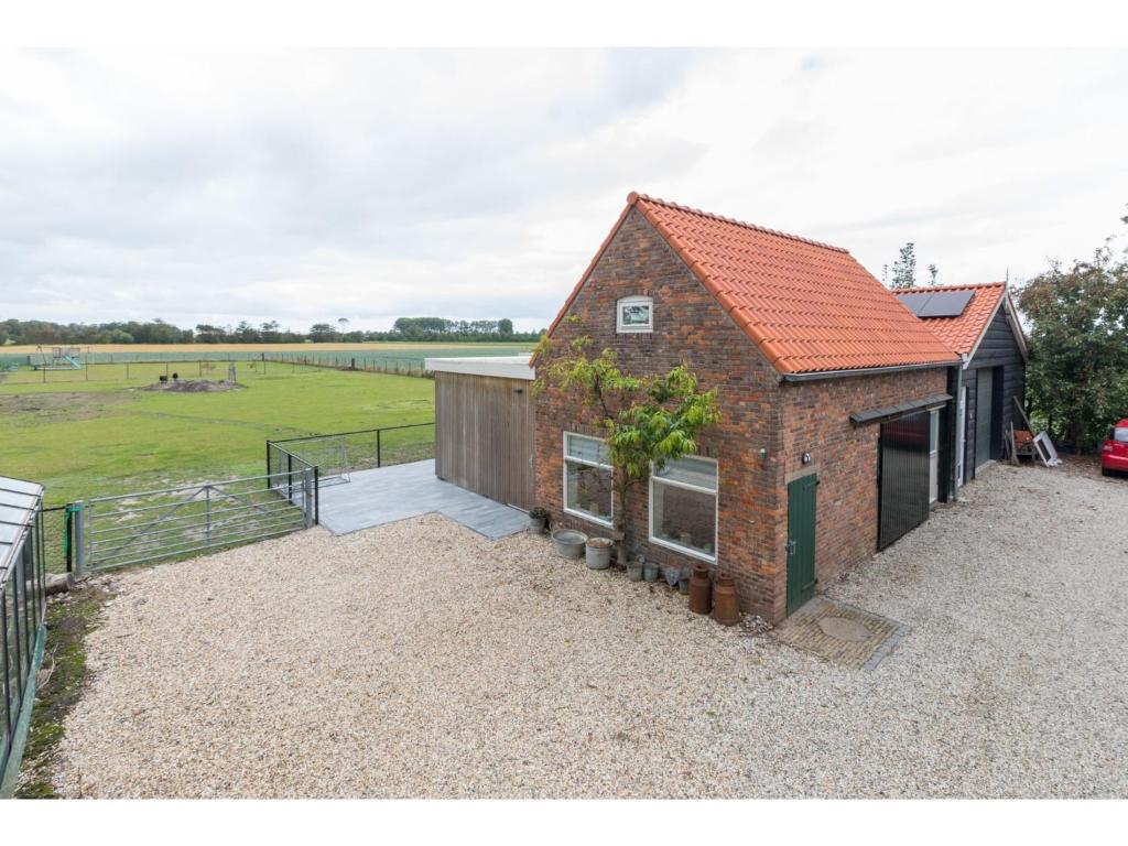 een stenen huis met een oranje dak en een veld bij Wonderfully quiet location in the polder pets allowed close to the beach in Koudekerke