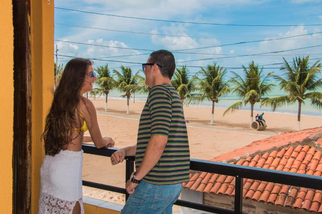 un homme et une femme debout sur un balcon regardant la plage dans l'établissement Pousada Praia Dos Encantos, à Japaratinga
