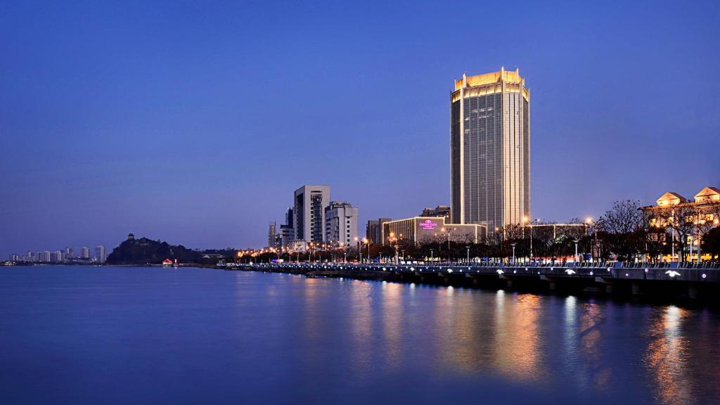 Crowne Plaza Zhenjiang, an IHG Hotel في تشنجيانغ: مدينة بالليل فيها نهر ومباني