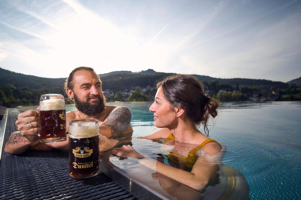 un uomo e una donna in una piscina con birra di Wander- und Aktivhotel Adam Bräu a Bodenmais