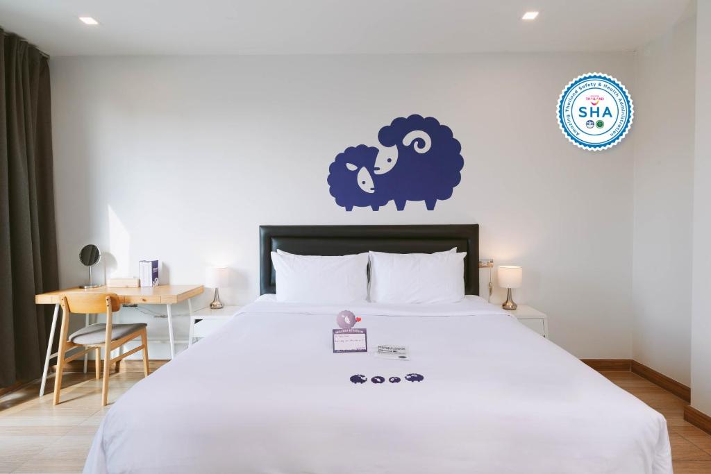 - une chambre dotée d'un lit blanc avec un mouton bleu sur le mur dans l'établissement Kokotel Bangkok Sukhumvit 50 - SHA Extra Plus, à Bangkok