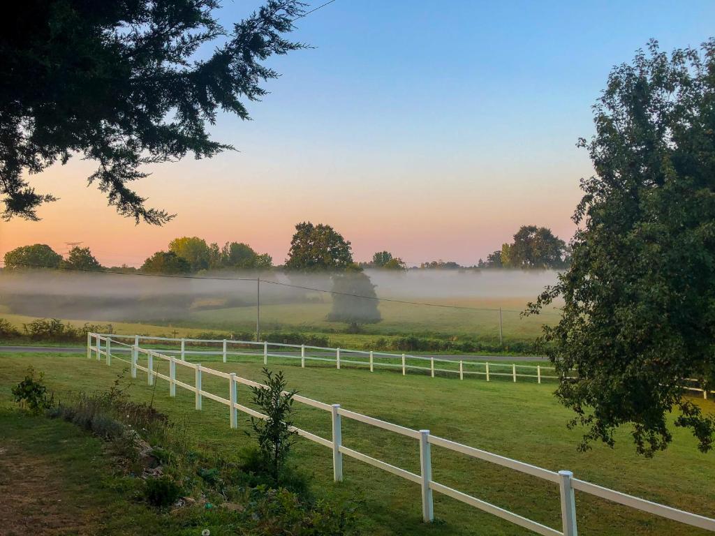 a white fence in a field with fog in the background at La Canopée du Mont in Saint-Georges-de-Reintembault