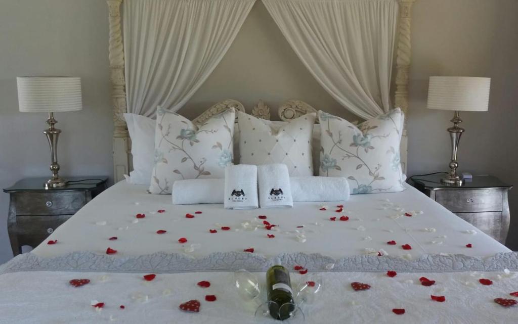 a white bed with red rose pedals on it at Slaley Country House in Stellenbosch