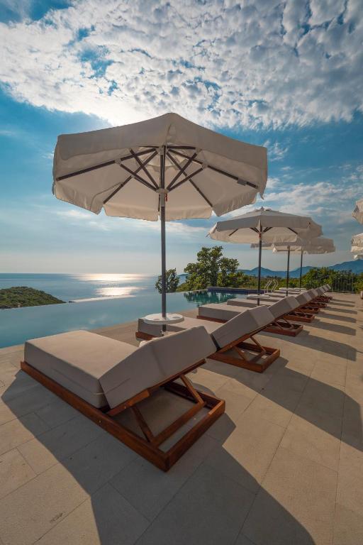 a row of lounge chairs with umbrellas on a patio at Vivid Blue Serenity Resort in Sveti Stefan