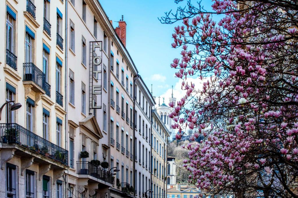 a city street with buildings and a tree with pink flowers at Hôtel Des Artistes in Lyon