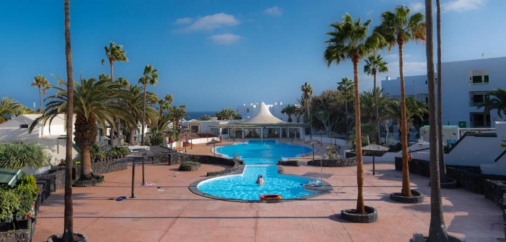 a fountain in a park with palm trees and a building at luxury casa playa roca bord de mer in Costa Teguise