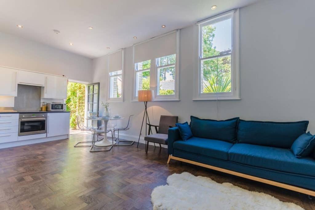 Una sala de estar con un sofá azul y una cocina. en Classroom Flat Suite in a converted school in Fowey town centre, en Fowey