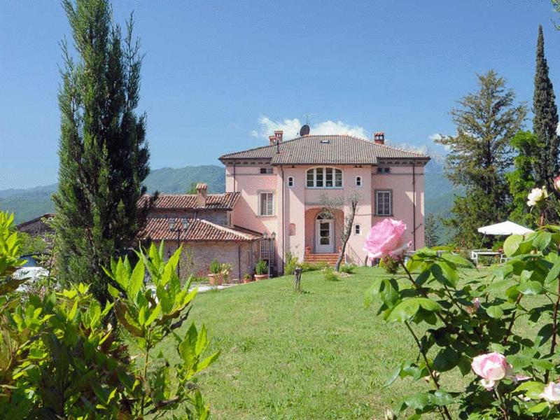 une grande maison rose sur un champ herbeux dans l'établissement Villa Belvedere, à Pieve Fosciana
