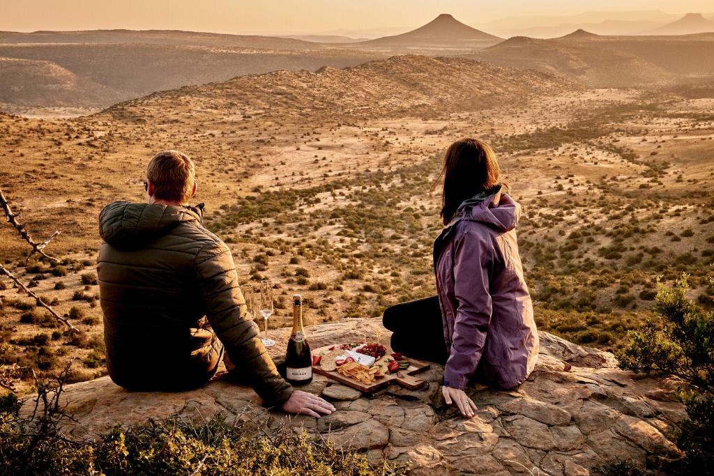 un homme et une femme assis sur un rocher avec une bouteille de vin dans l'établissement Glen Harry Game Reserve, à Graaff-Reinet