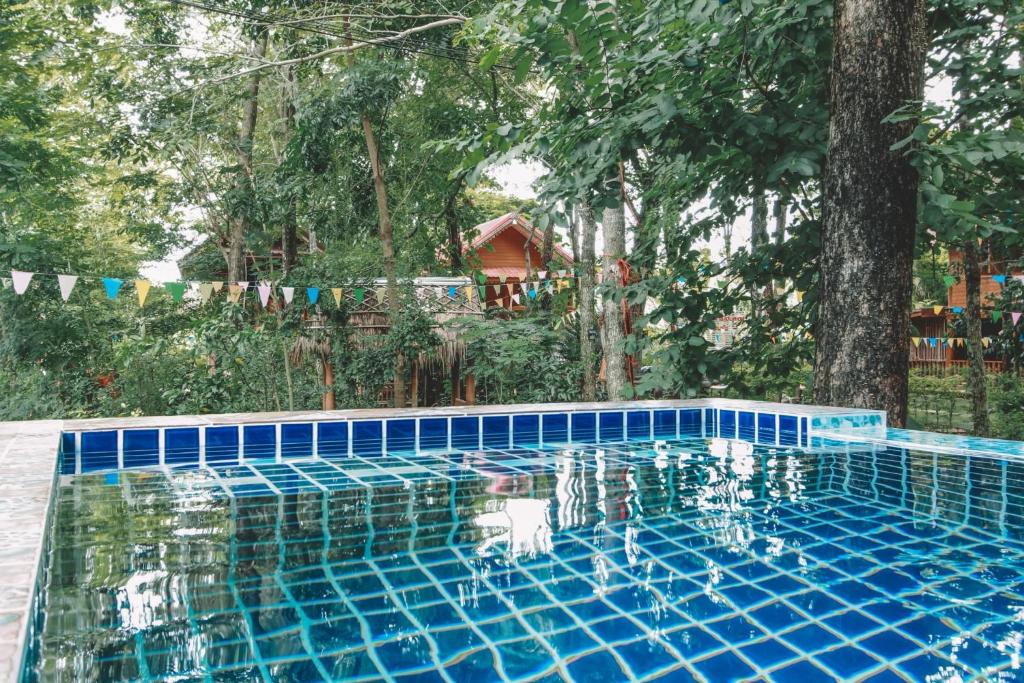 una piscina de azulejos azules con árboles en el fondo en Akchanok Homestay, en Phitsanulok