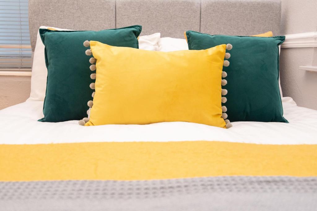 a bed with a yellow pillow and green pillows at The Harrogate Abode in Harrogate