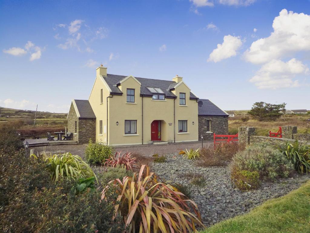 a large yellow house with a red door in a field at Fourteens Holiday Home Ballinskelligs in Ballinskelligs