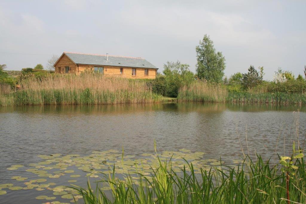 a house sitting on the side of a lake with lilies at Berry Barns in Shebbear