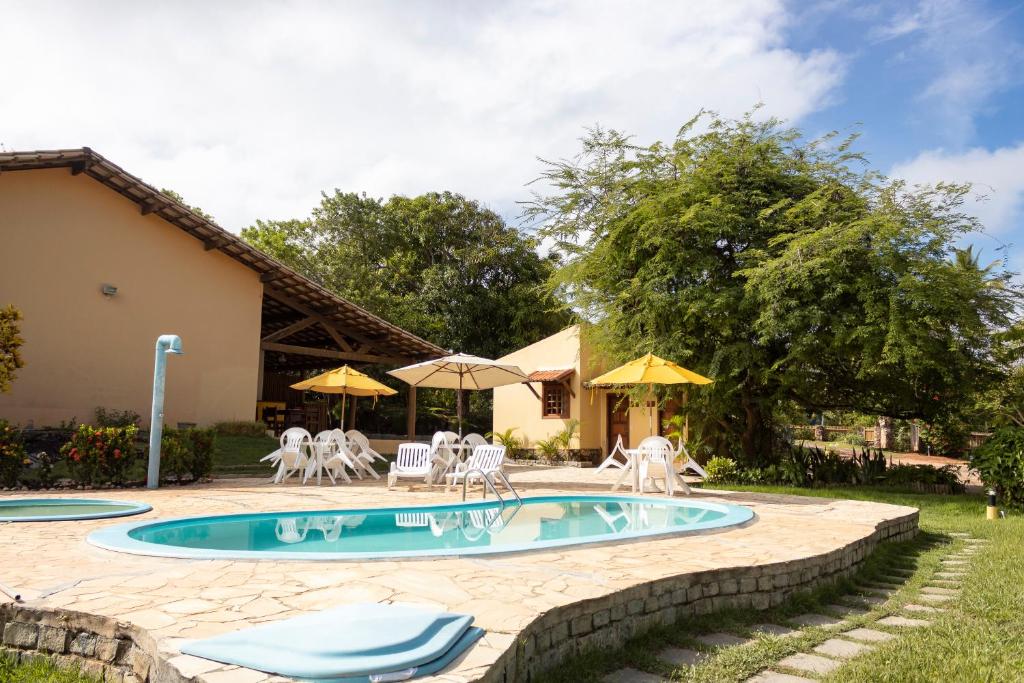 a pool with chairs and umbrellas next to a house at Pousada Lagoa Da Pedra in Imbassai