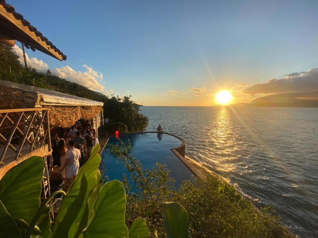 una piscina junto al agua con la puesta de sol en Magnífica Costeira, en Ilhabela