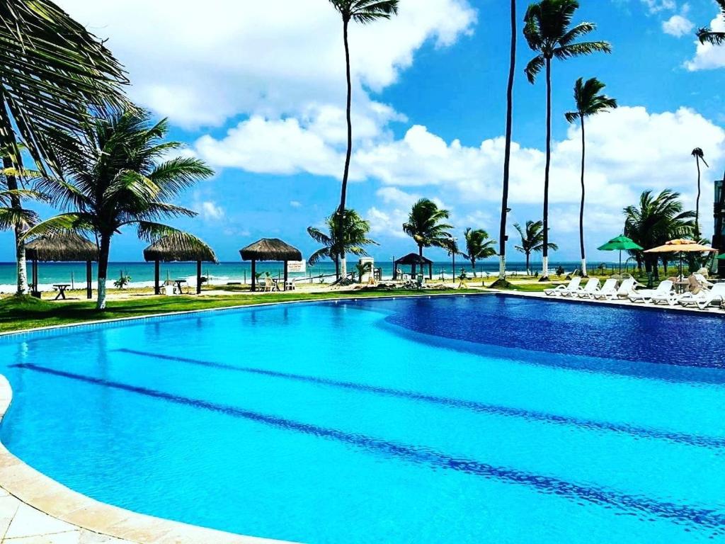 a swimming pool next to a beach with palm trees at Ancorar Resort em Porto de Galinhas in Porto De Galinhas