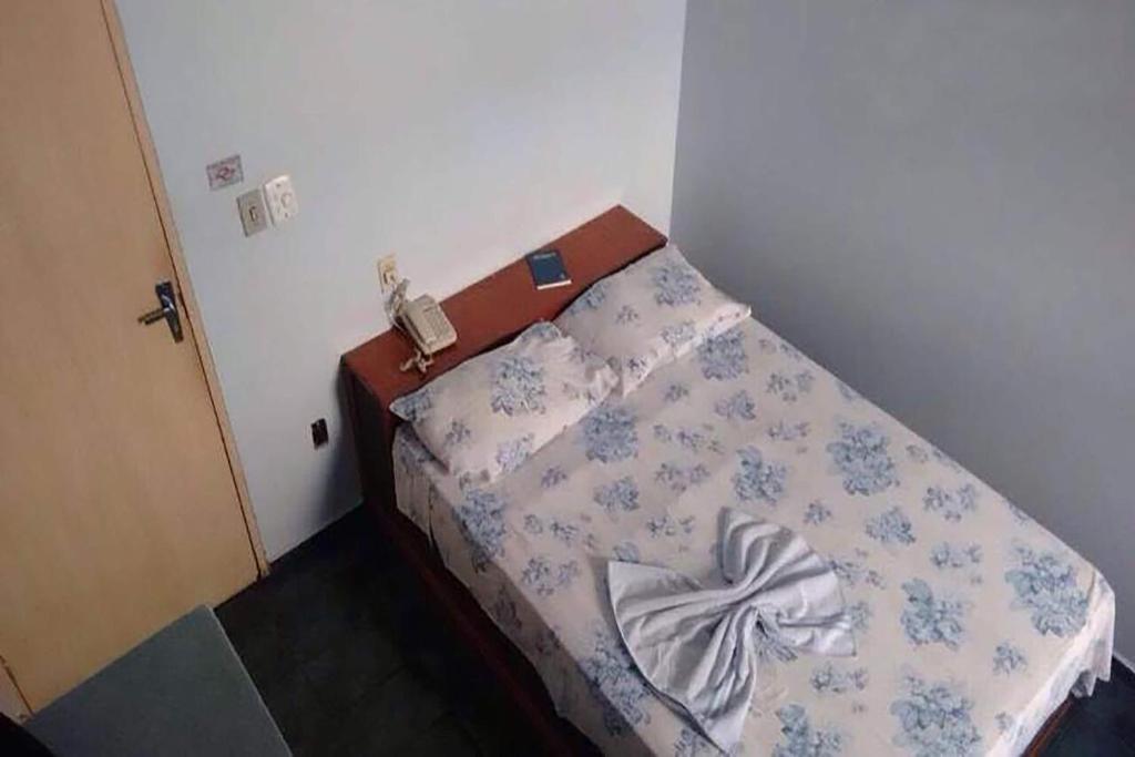 Cama en habitación pequeña con teléfono en Hotel Pousa La, en Cosmópolis