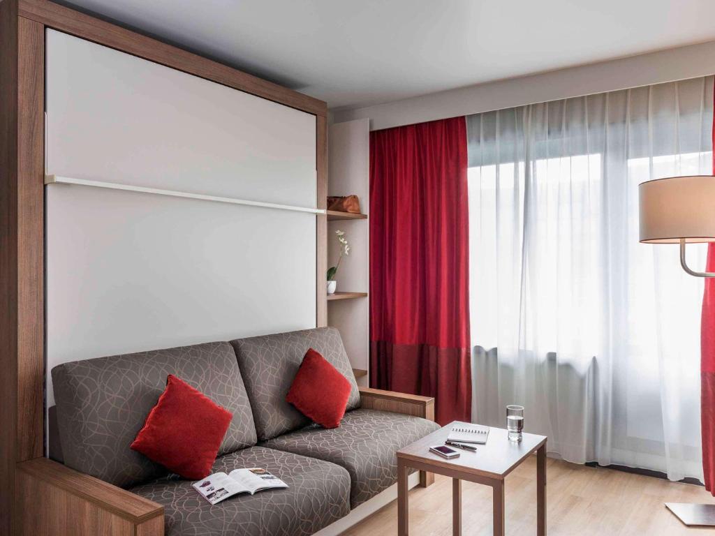 - un salon avec un canapé gris et des oreillers rouges dans l'établissement Aparthotel Adagio Paris Bercy Village, à Paris