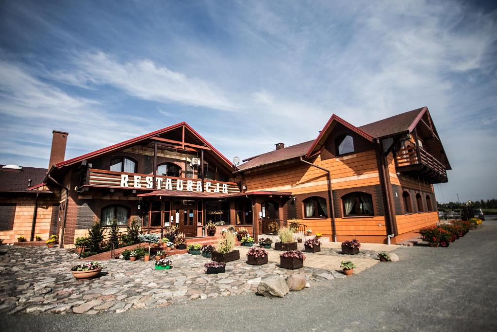 a large wooden building with potted plants in front of it at Hotel Trzy Podkowy*** in Biskupiec