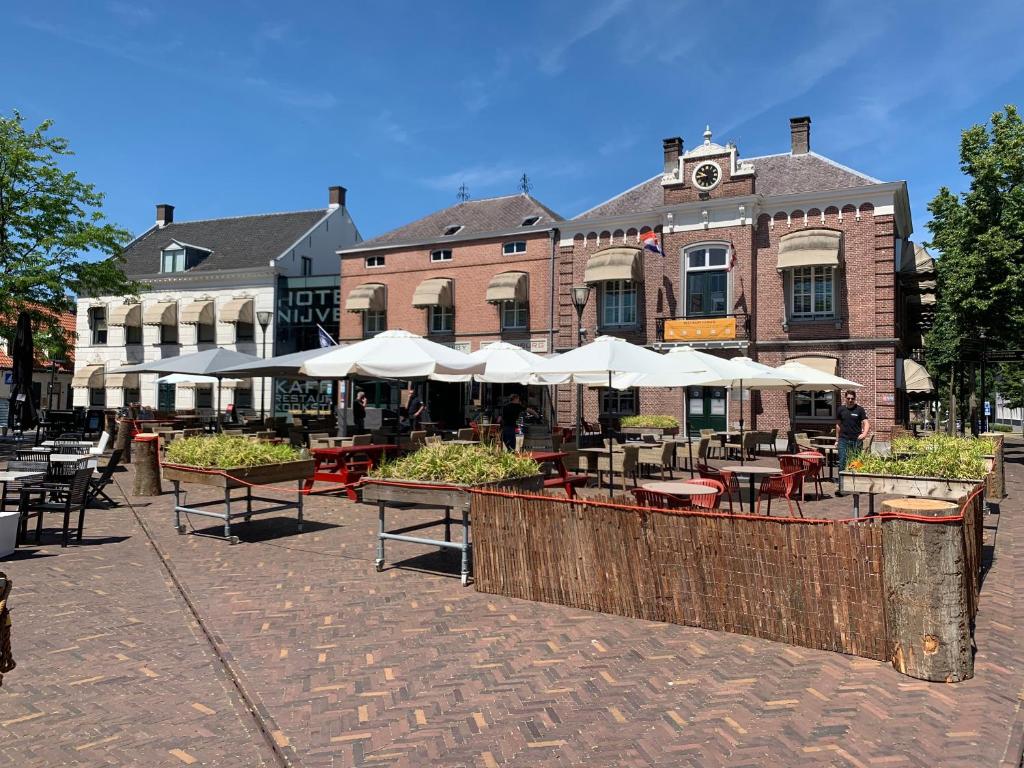 a cafe with tables and white umbrellas in front of a building at Hotel Nijver in Geldrop