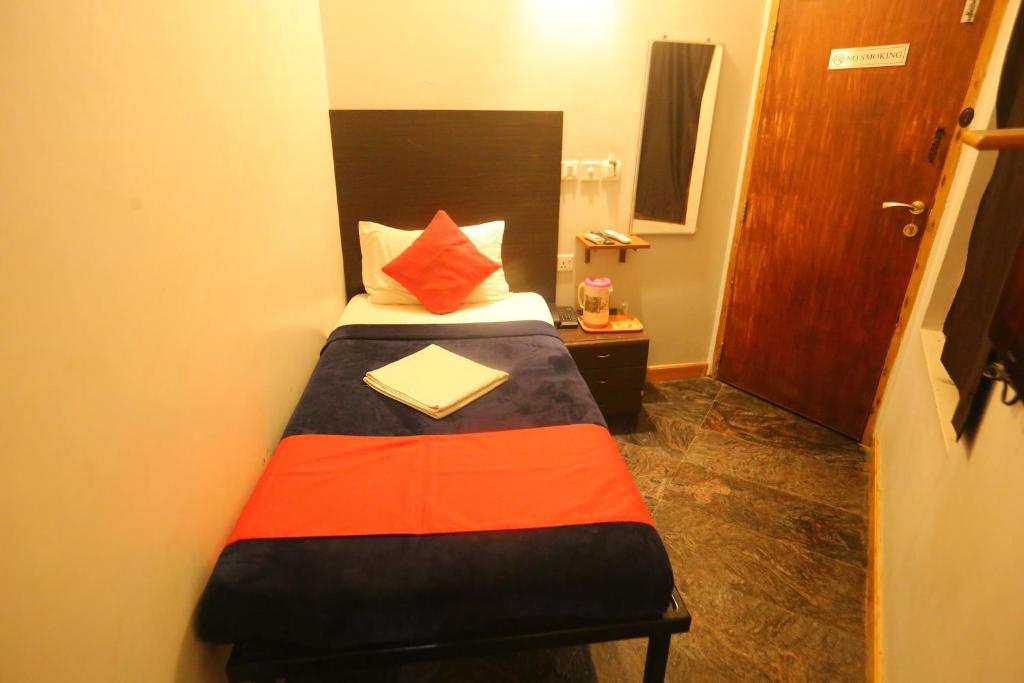 een kleine slaapkamer met een bed met een oranje en zwarte deken bij Le Apex Home Stay in Auroville