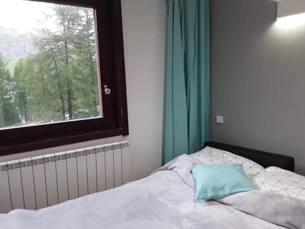 łóżko z niebieską poduszką w pokoju z oknem w obiekcie Alfastudio w mieście Breuil-Cervinia