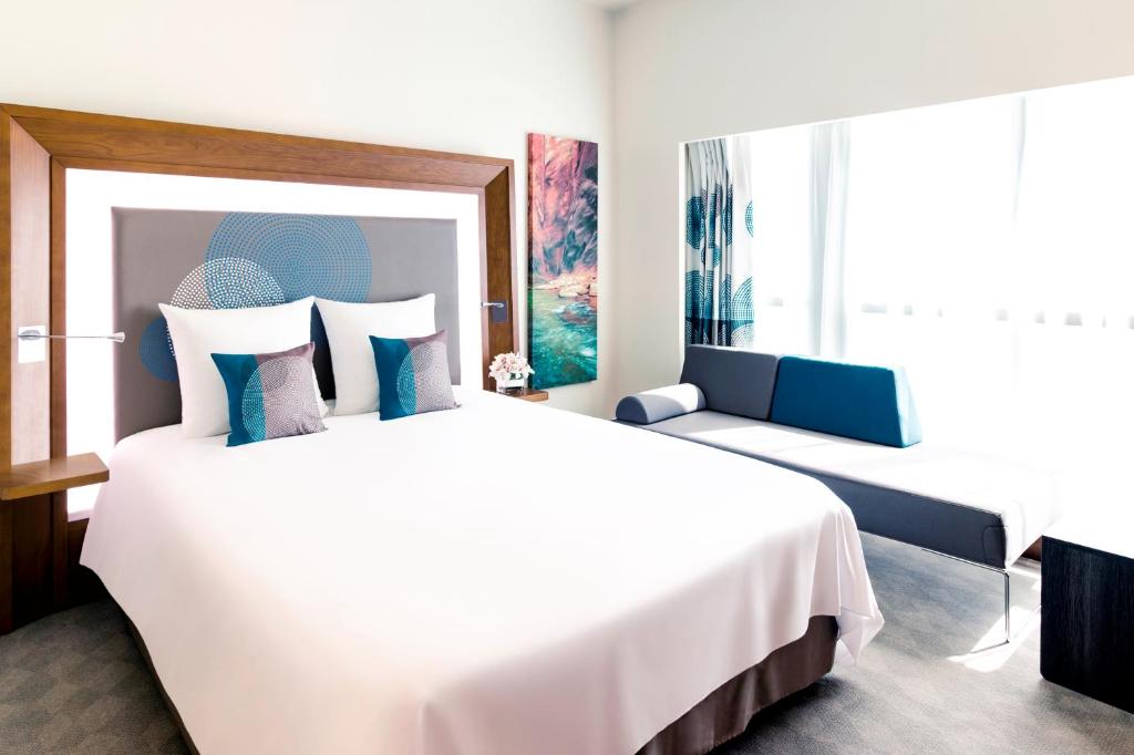a bedroom with a large white bed with blue pillows at Novotel Fujairah in Fujairah