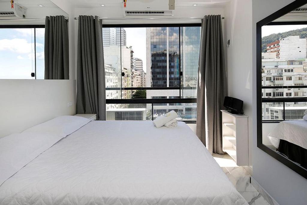 a bedroom with a white bed and a large window at Studio moderno com vista privilegiada para a praia in Rio de Janeiro