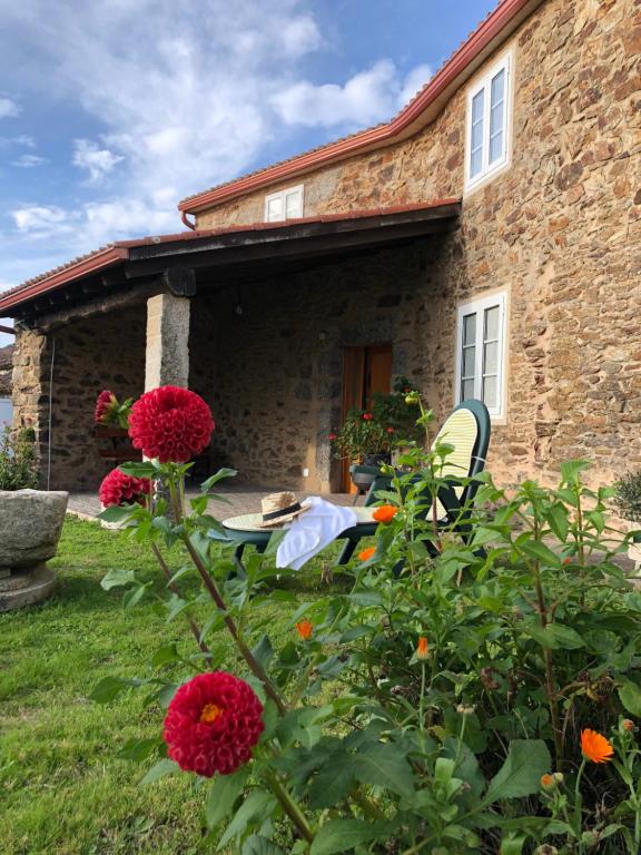 una casa de piedra con una mesa y flores en el patio en VUT Rural - Boente en Arzúa