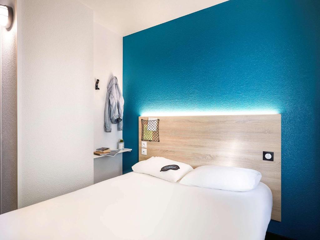 een wit bed in een kamer met een blauwe muur bij hotelF1 Mulhouse Centre Ouest in Mulhouse