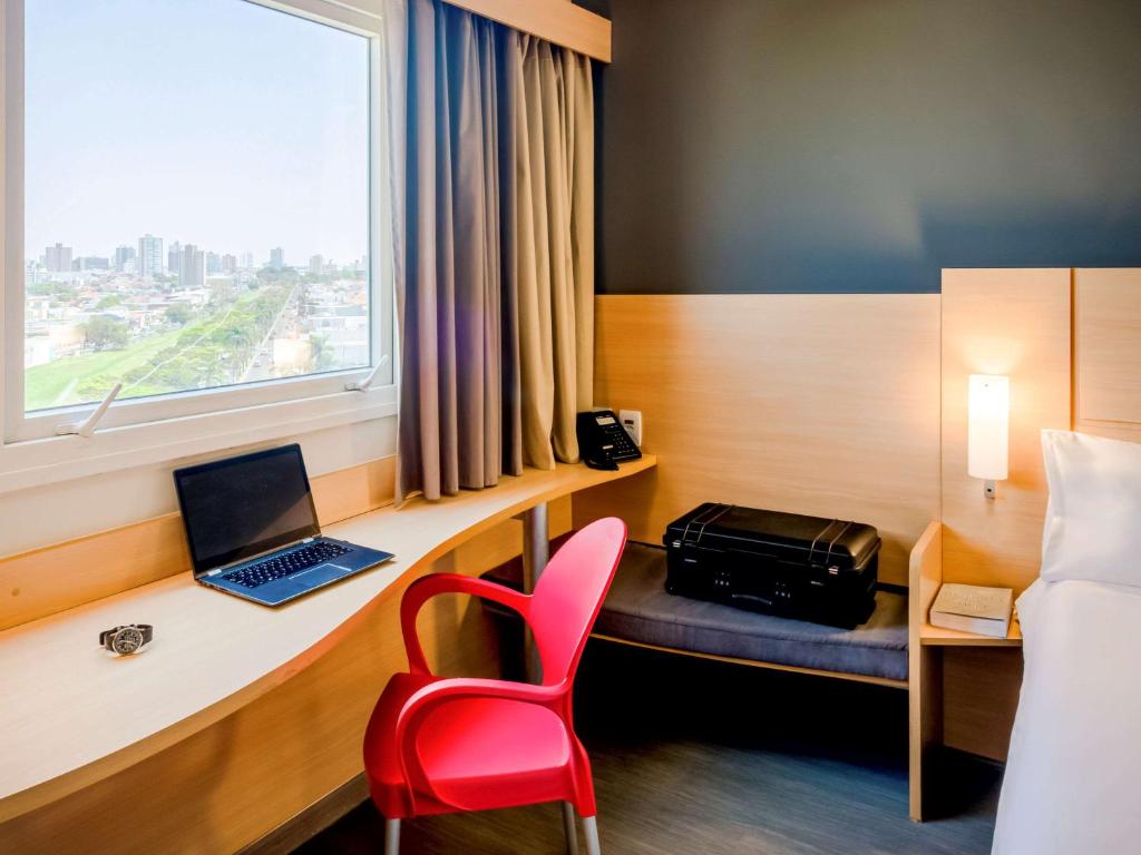 um quarto com uma secretária com um computador portátil e uma cadeira vermelha em ibis Marilia em Marília