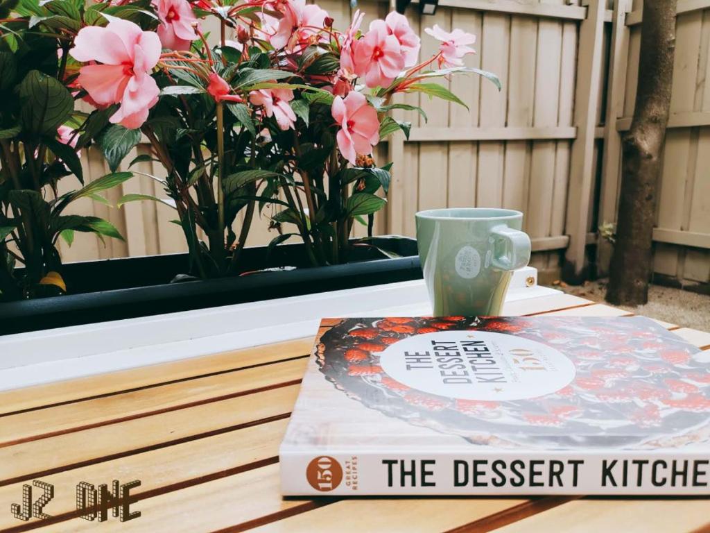 a book and a cup on a table with flowers at JZ One in Box Hill