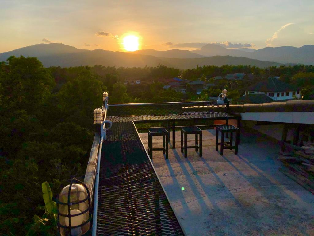 a sunset on the roof of a building with tables and chairs at Sandee Place Mountain View Hotel โรงแรมแสนดีเพลส เมาเท่นวิว จอมทอง in Chom Thong