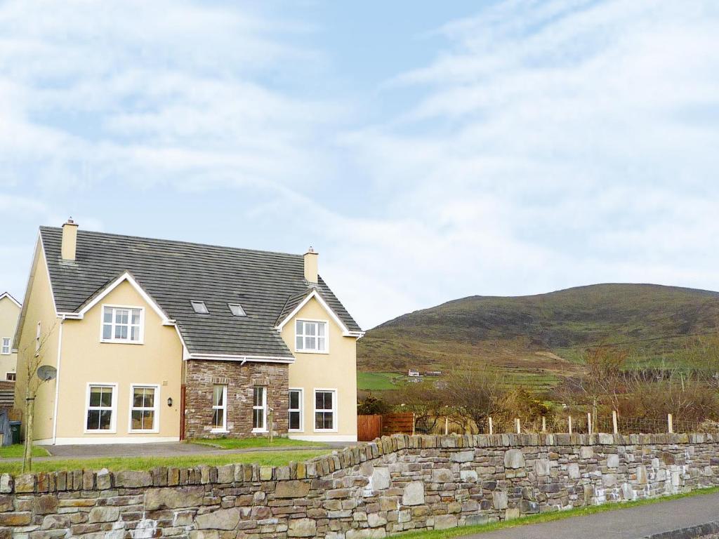 a house with a stone wall and mountains in the background at Cois Chnoic Holiday Home Dingle in Dingle