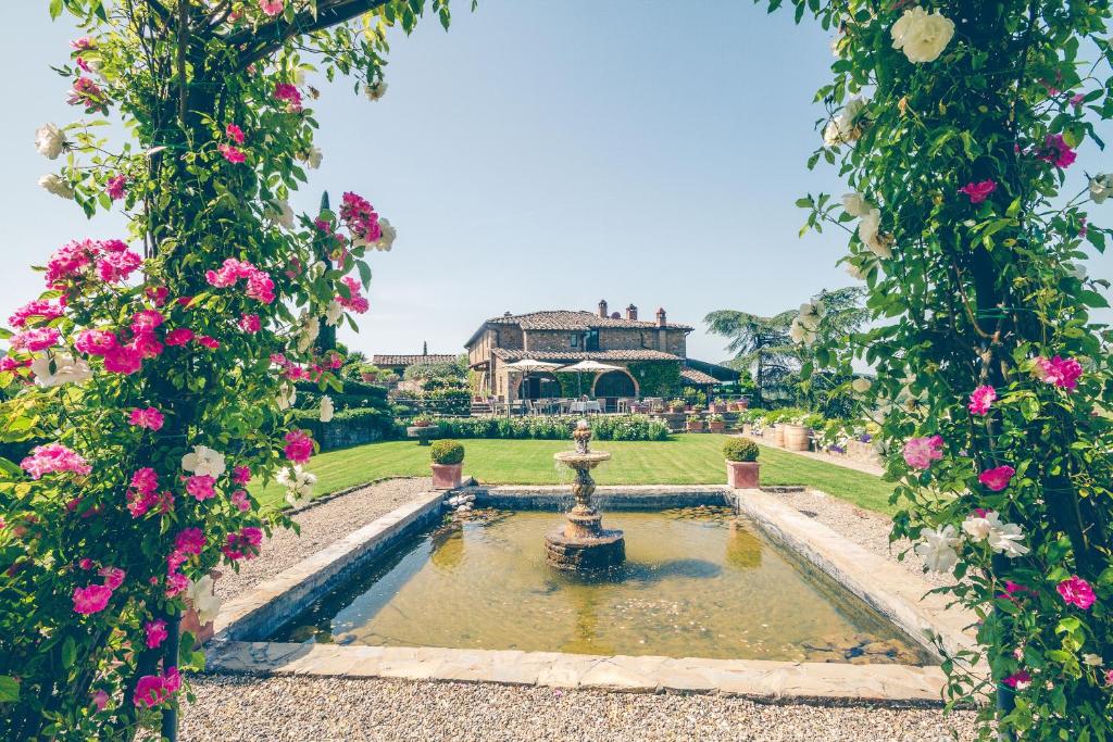 a garden with a fountain in front of a house with pink flowers at Capannelle Wine Resort in Gaiole in Chianti