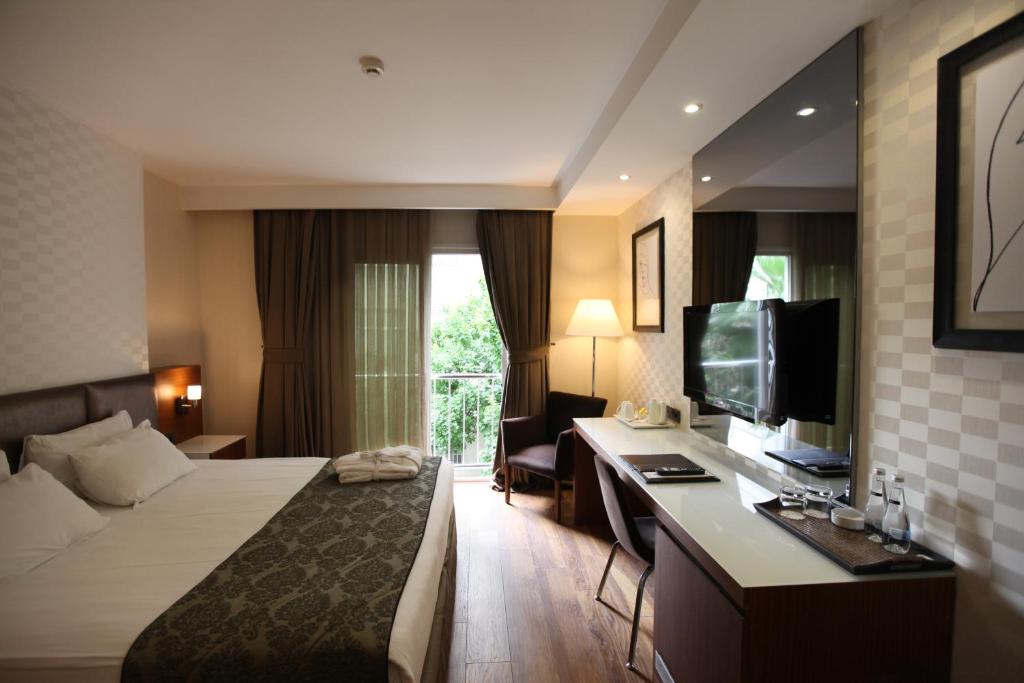 アダナにあるRiva Reşatbey Luxury Hotelのベッド、デスク、テレビが備わるホテルルームです。