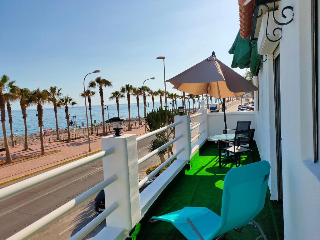 un balcón con sillas y sombrilla y la playa en Tranquila casa frente al mar en Adra