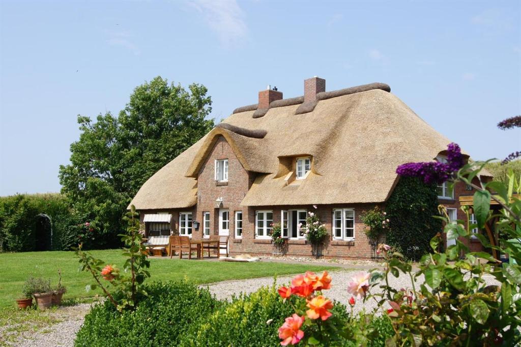 ein Haus mit einem Strohdach und einem Garten in der Unterkunft Reetkate Kaltenhoern in Tetenbüll