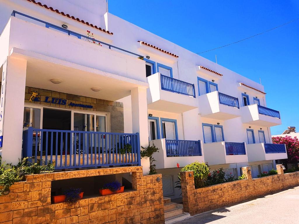 ein großes weißes Gebäude mit blauen Balkonen darauf in der Unterkunft Luis Apartments in Mastichari