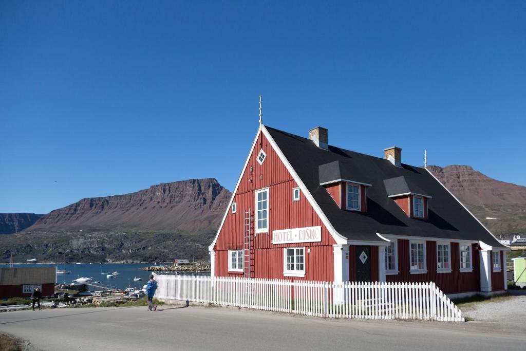 un hombre parado frente a una casa roja en Hotel Disko Island en Qeqertarsuaq