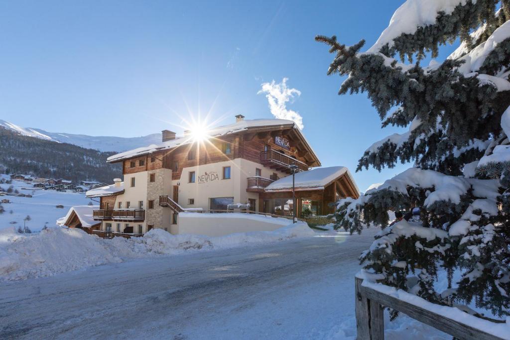 a house in the snow with the sun shining on it at Mont Chalet Nevada - Hotel & Spa in Livigno