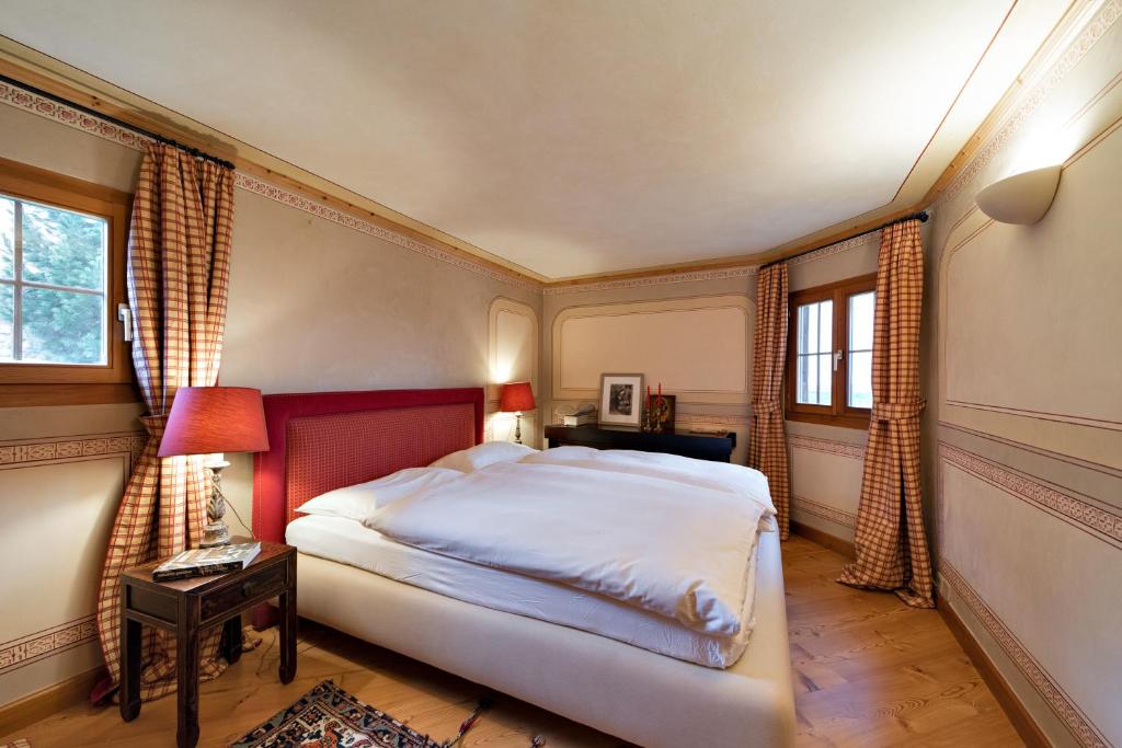 a bedroom with a large bed and two windows at Chesa Romana - Silvaplana in Silvaplana