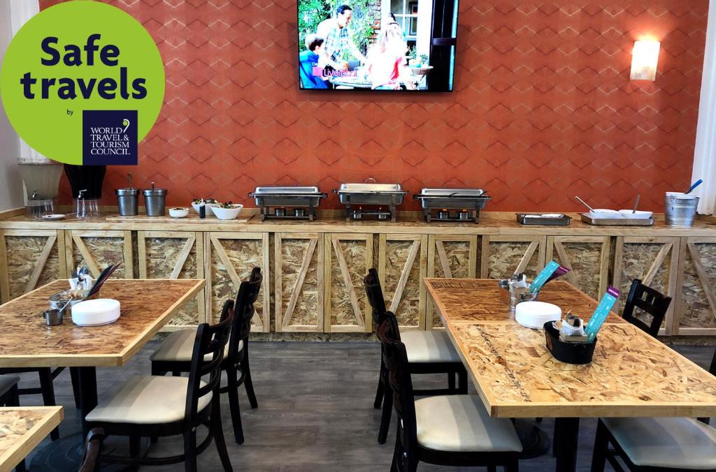 A casual breakfast room with buffet chafing dishes, dining tables, and a wall-mounted television.