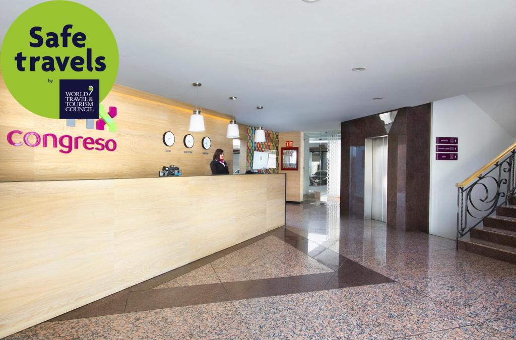 A broad reception lobby has a wood-fronted desk, elevators, stairs, and polished stone flooring.