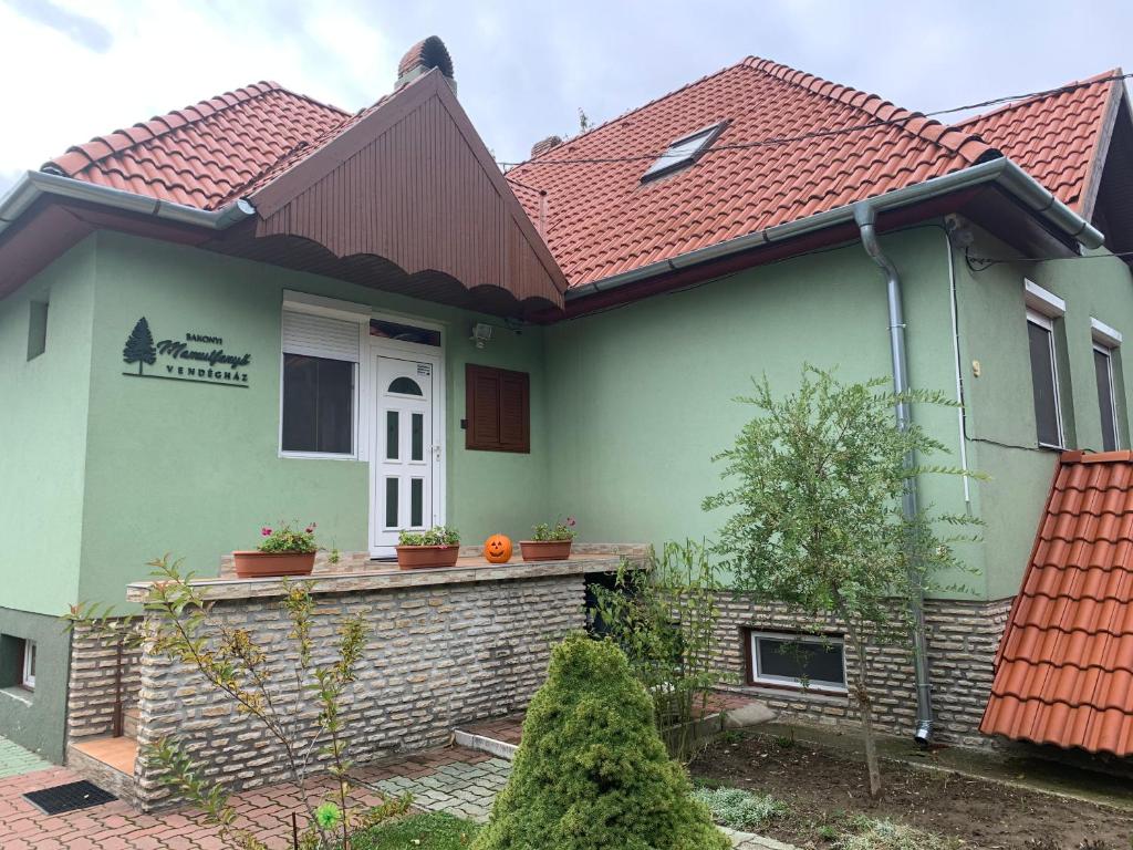 a green house with a red roof at Bakonyi Mamutfenyő Vendégház in Tés