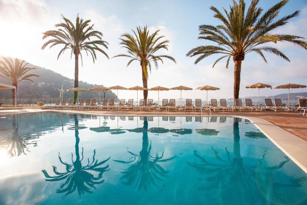 einen Pool mit Palmen und Sonnenschirmen in der Unterkunft Grupotel Imperio Playa in Sant Joan de Labritja