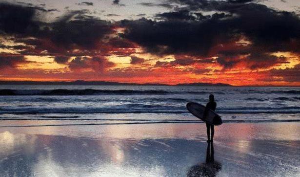 un hombre de pie en una playa sosteniendo una tabla de surf en Golden's Cove Apartments at Sneem Hotel, en Sneem