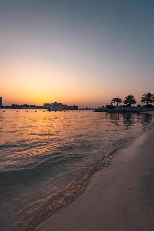 a beach with palm trees and the ocean at sunset at Traders Hotel, Abu Dhabi in Abu Dhabi